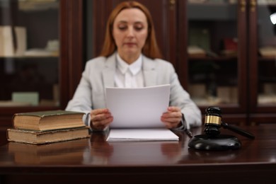 Photo of Judge working with documents at wooden table in office, focus on gavel