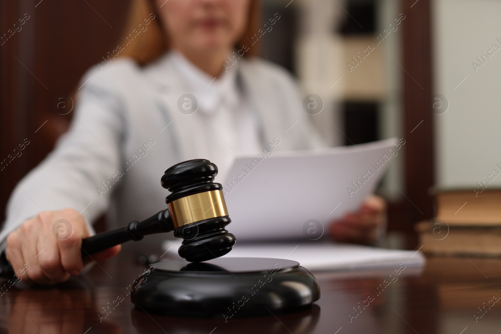 Photo of Judge with document striking gavel at table in office, closeup