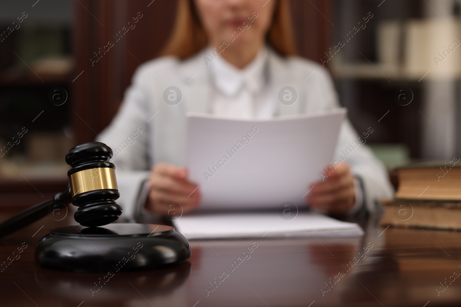 Photo of Judge working with documents at wooden table in office, focus on gavel