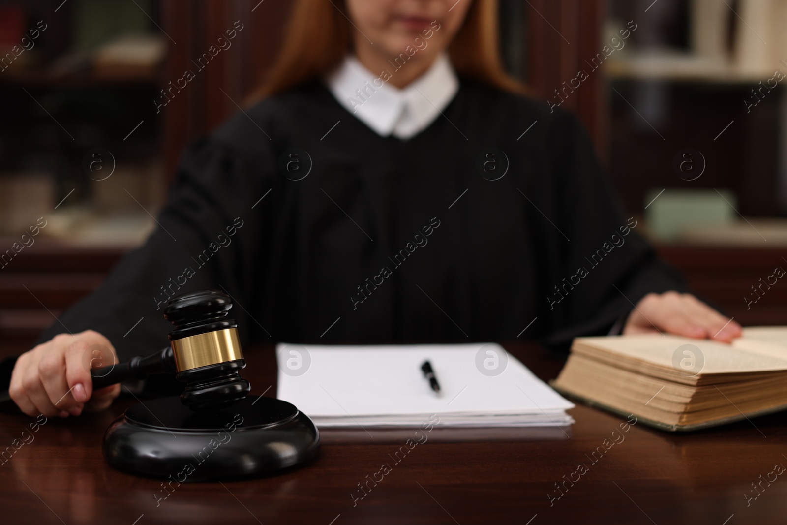 Photo of Judge with document striking gavel at wooden table in office, closeup