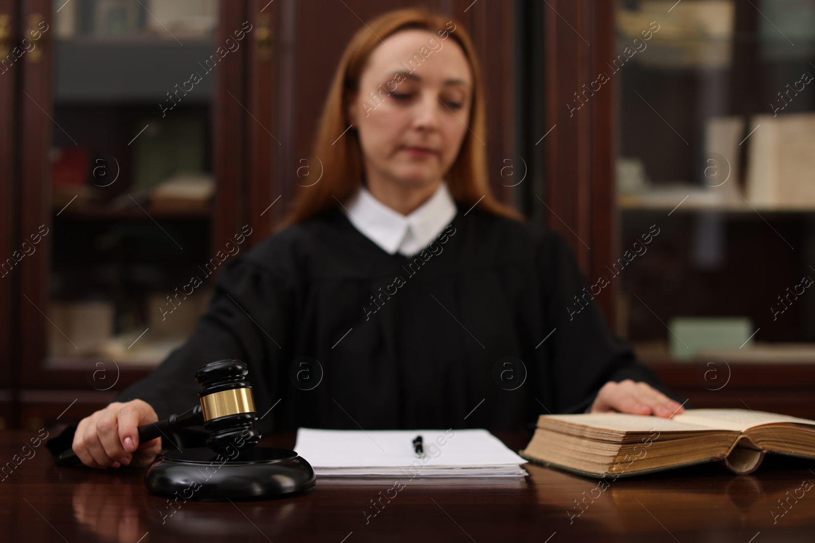 Photo of Judge with document striking gavel at wooden table in office, selective focus