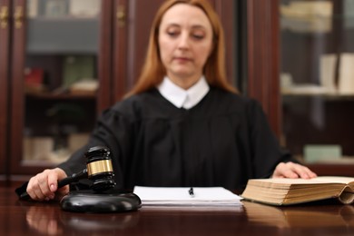 Photo of Judge with document striking gavel at wooden table in office, selective focus