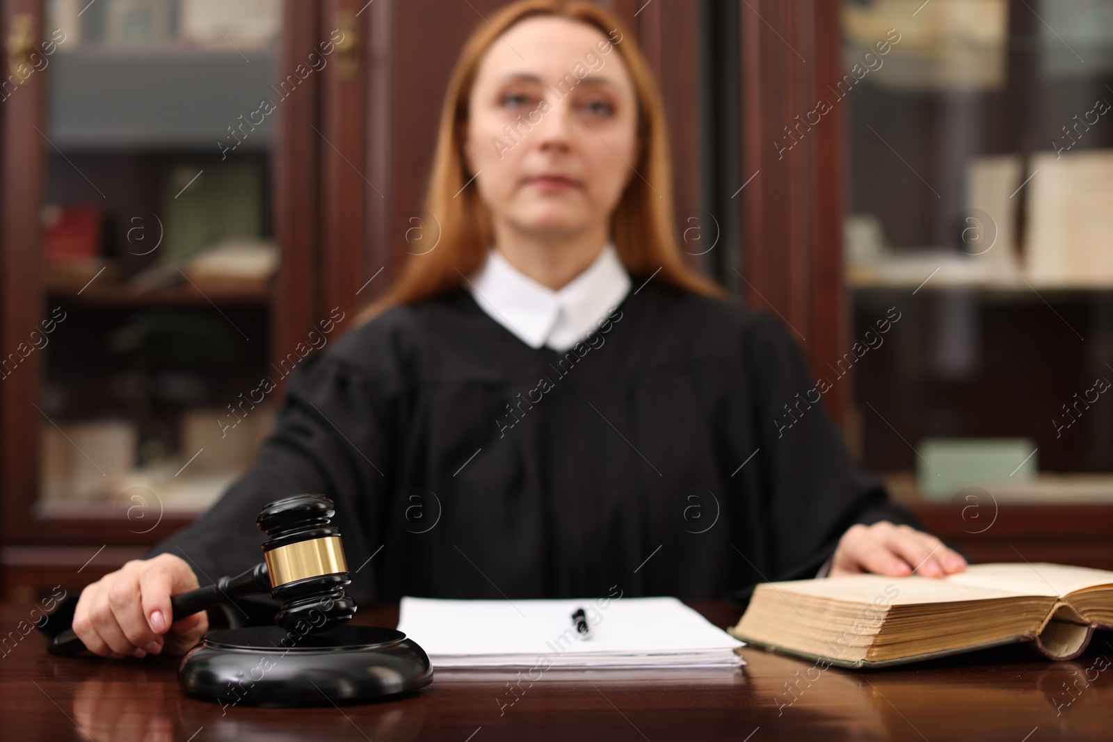 Photo of Judge with document striking gavel at wooden table in office, selective focus