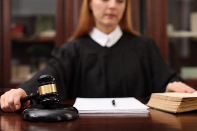 Photo of Judge with document striking gavel at wooden table in office, selective focus