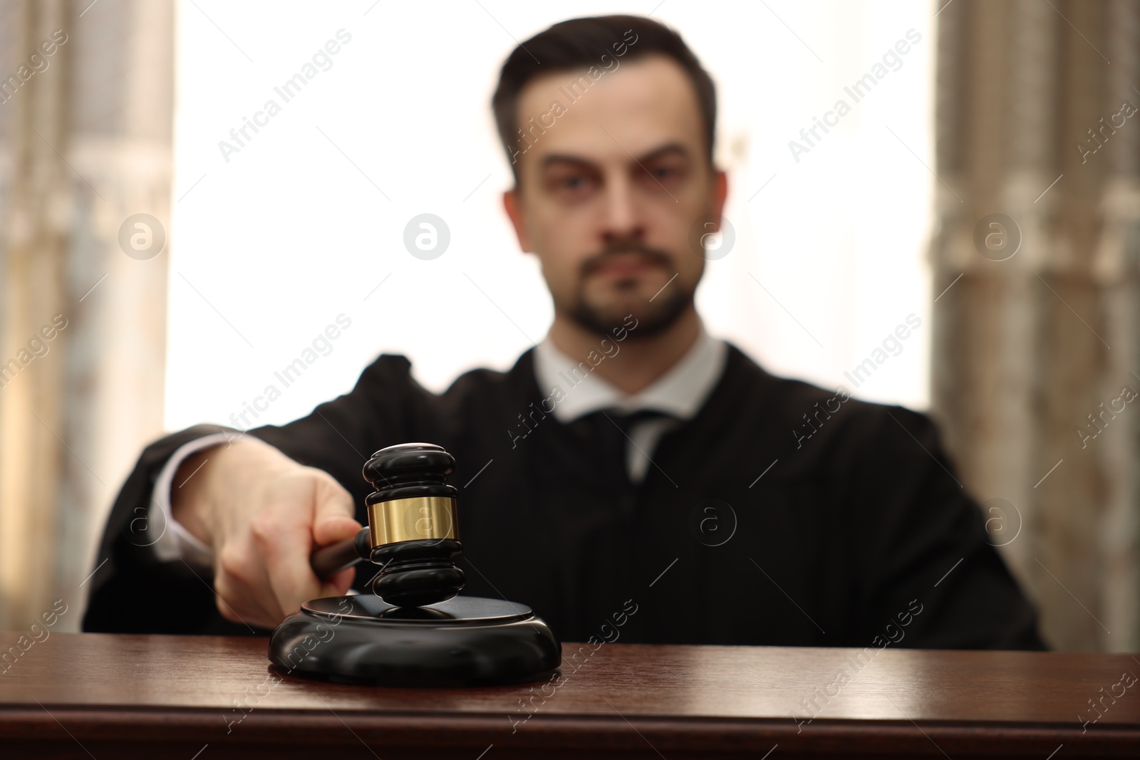 Photo of Judge striking gavel at wooden table in courtroom, selective focus