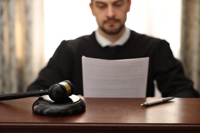 Photo of Judge with document at wooden table in office, focus on gavel