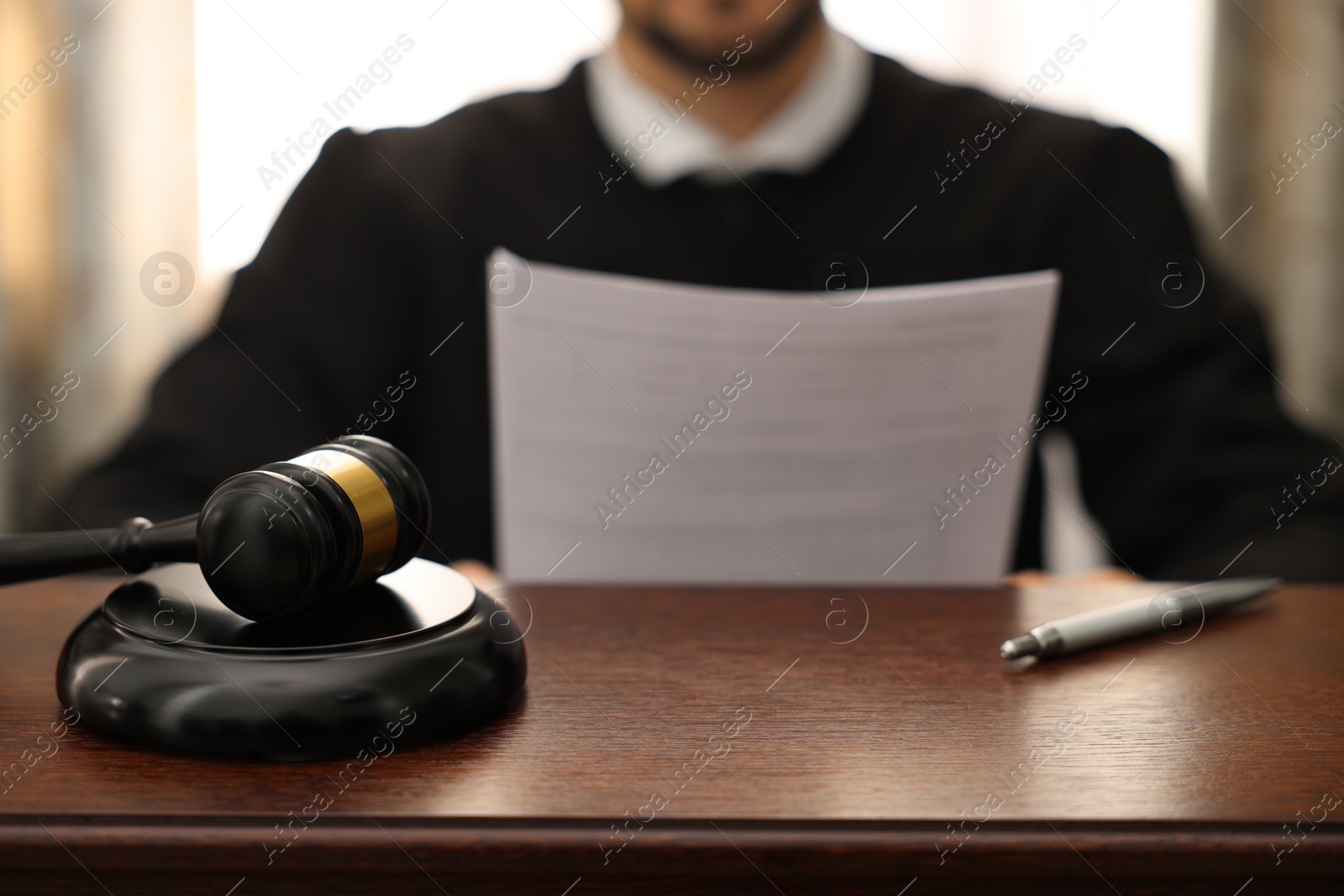 Photo of Judge with document at wooden table in office, focus on gavel