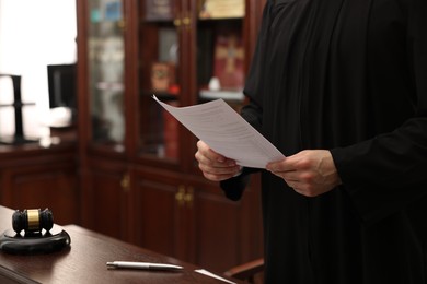 Photo of Judge with document at wooden table in courtroom, closeup. Space for text