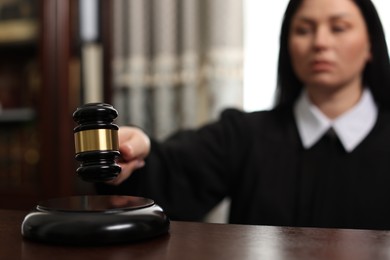 Photo of Judge striking gavel at wooden table in courtroom, selective focus