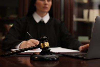 Photo of Judge working with laptop at wooden table in office, focus on gavel