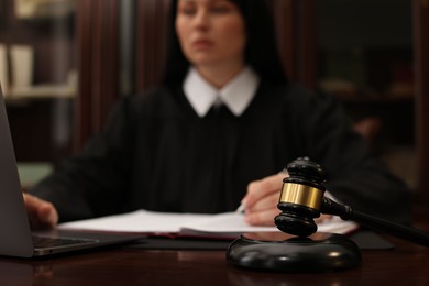 Photo of Judge working with laptop at wooden table in office, focus on gavel