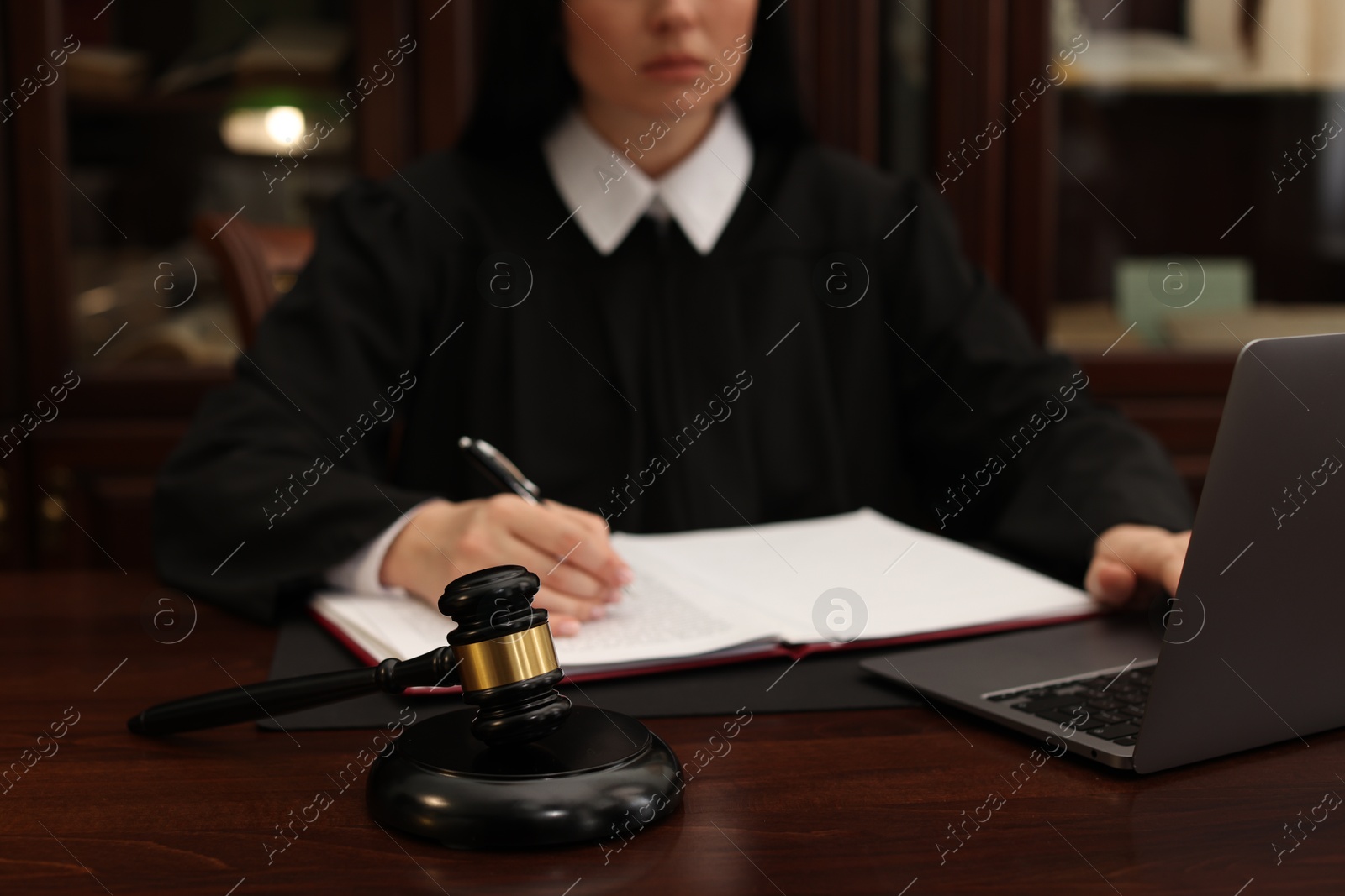 Photo of Judge working with laptop at wooden table in office, focus on gavel