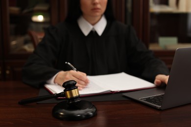 Photo of Judge working with laptop at wooden table in office, focus on gavel