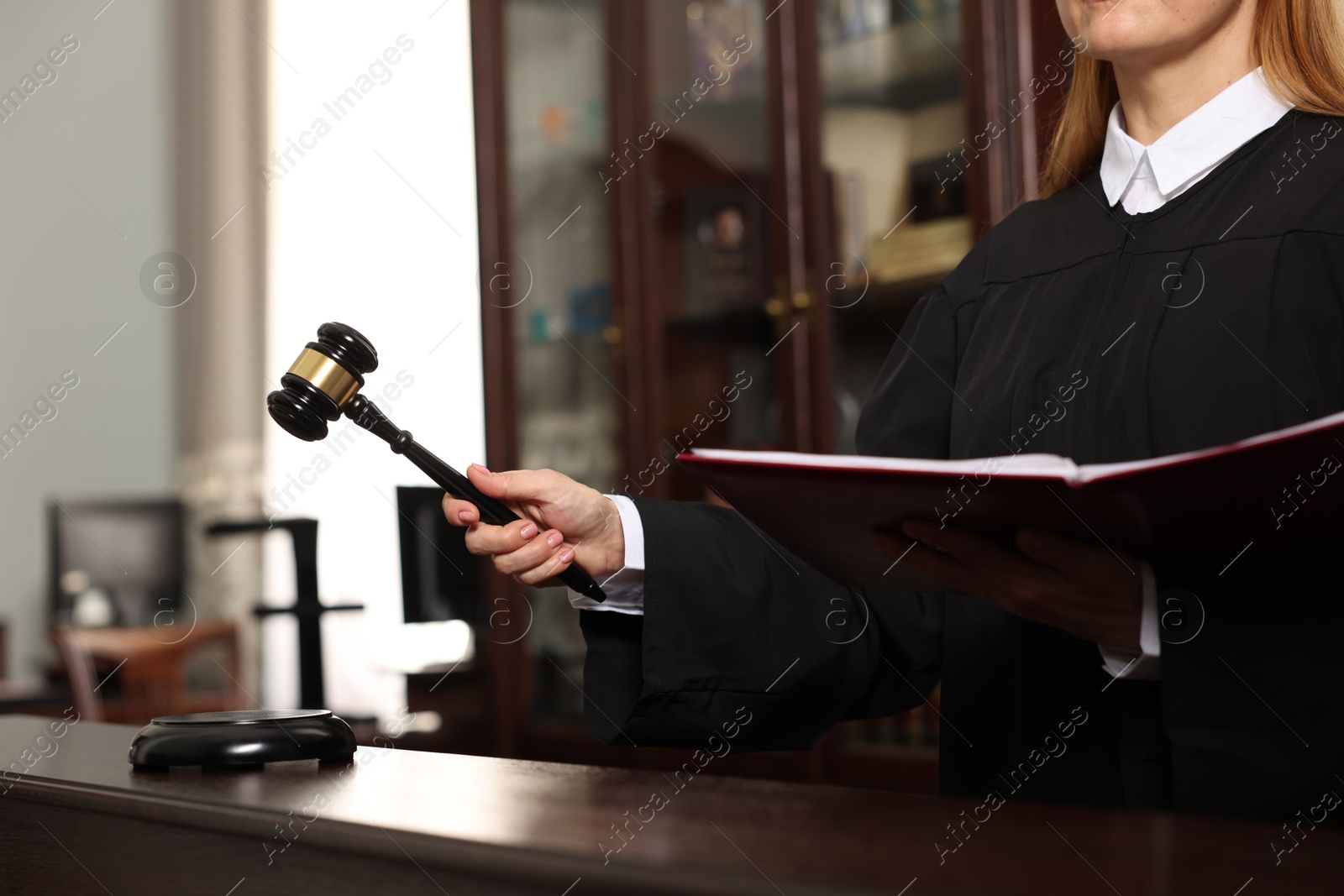 Photo of Judge with folder of documents striking gavel at table in courtroom, closeup