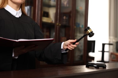 Photo of Judge with folder of documents striking gavel at table in courtroom, closeup