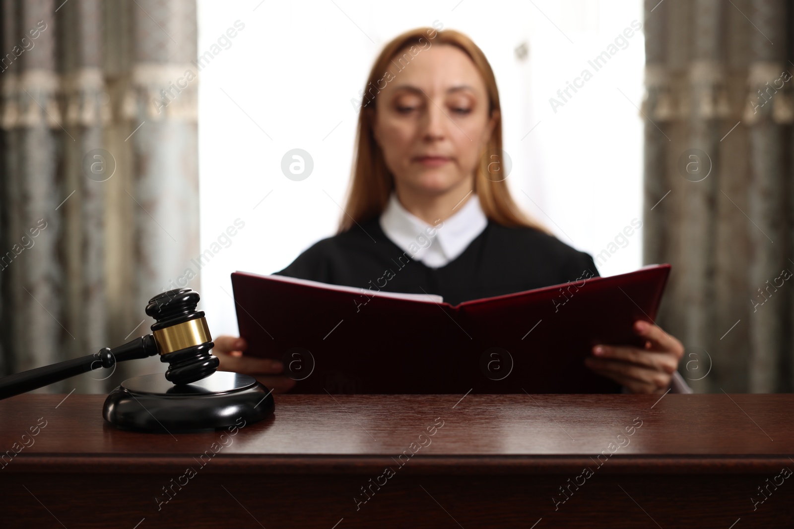 Photo of Judge with folder of documents at wooden table in courtroom, focus on gavel