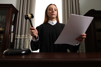 Photo of Judge with gavel and documents at table in courtroom, low angle view