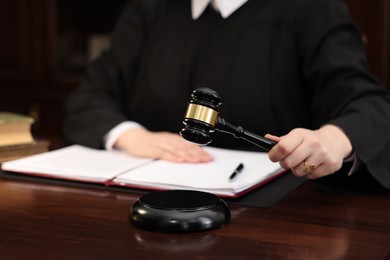 Photo of Judge striking gavel at wooden table in office, closeup