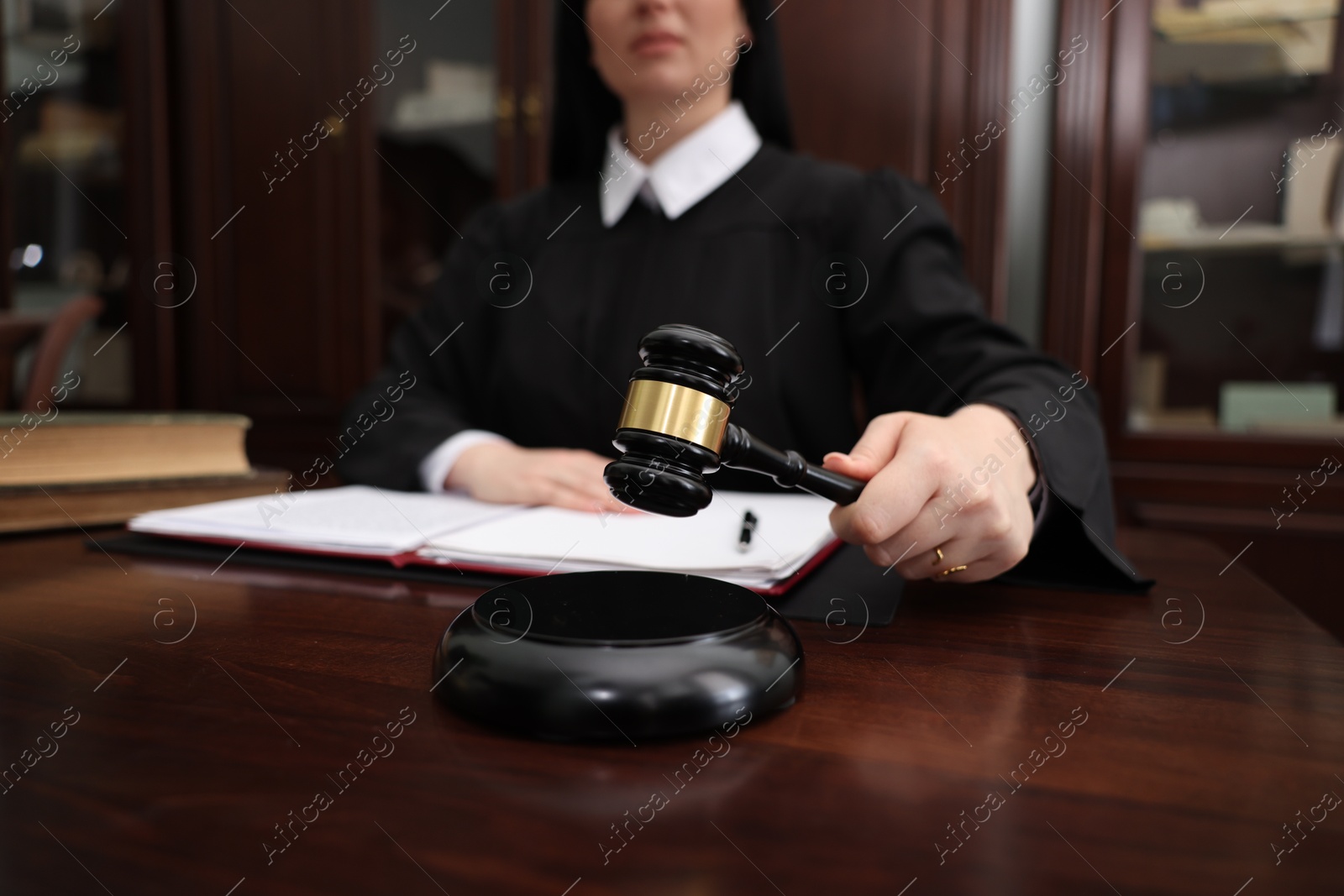 Photo of Judge striking gavel at wooden table in office, closeup