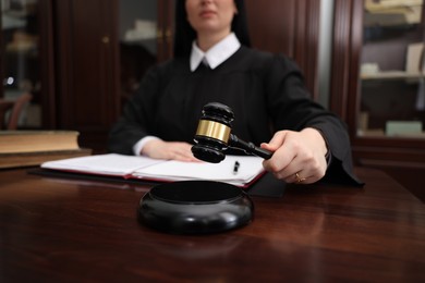 Photo of Judge striking gavel at wooden table in office, closeup