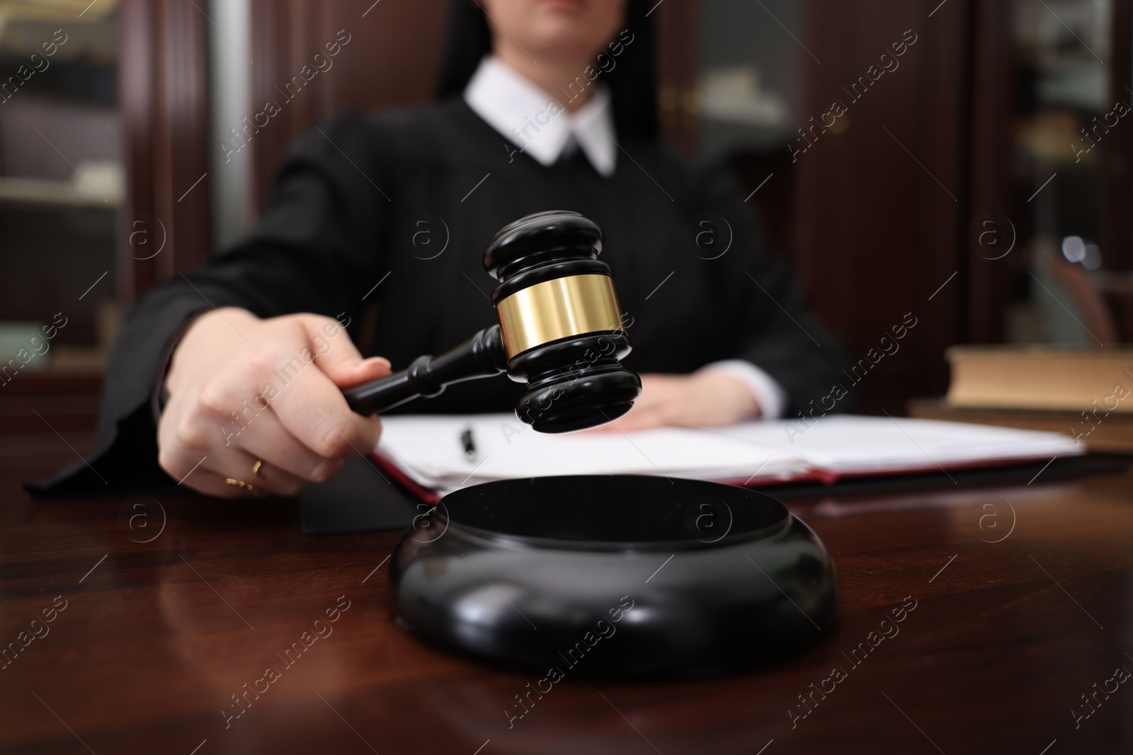 Photo of Judge striking gavel at wooden table in office, closeup