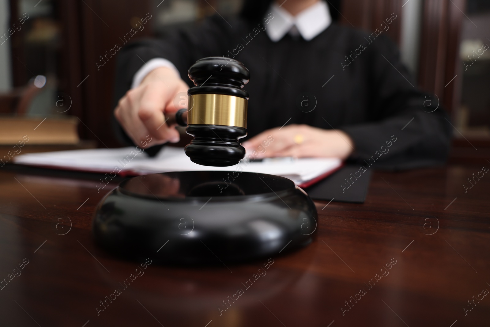 Photo of Judge striking gavel at wooden table in office, closeup