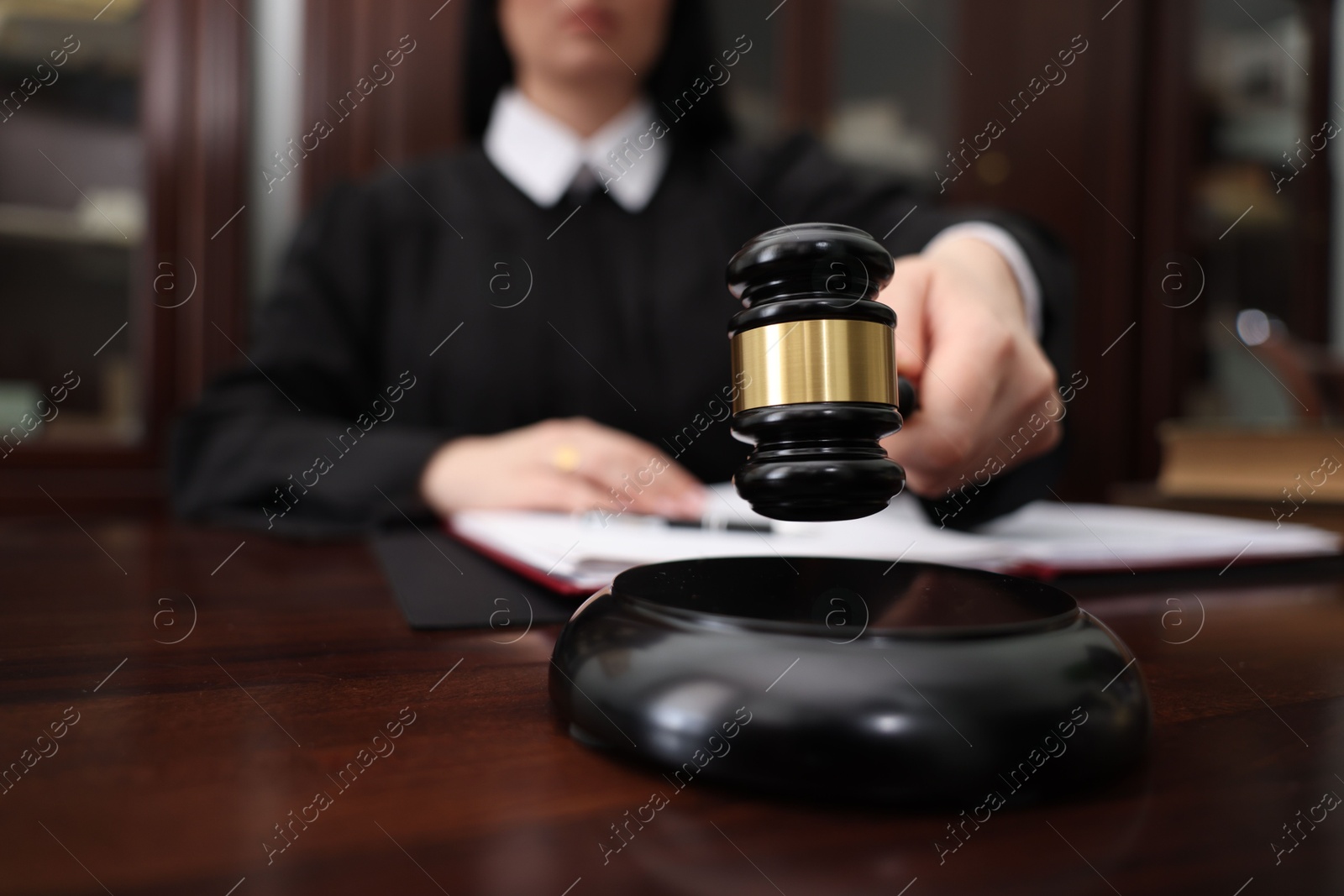 Photo of Judge striking gavel at wooden table in office, closeup