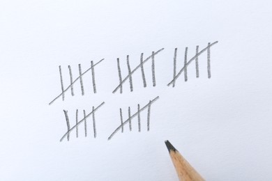 Photo of Counting days by drawing sticks with pencil on white background, closeup