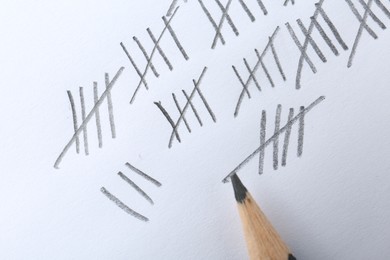 Photo of Counting days by drawing sticks with pencil on white background, closeup