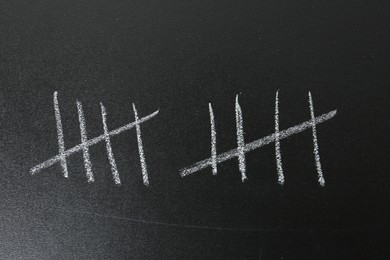 Photo of Counting days by drawing sticks with chalk on blackboard, closeup