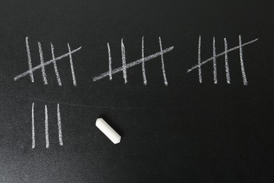 Photo of Counting days by drawing sticks with chalk on blackboard, closeup