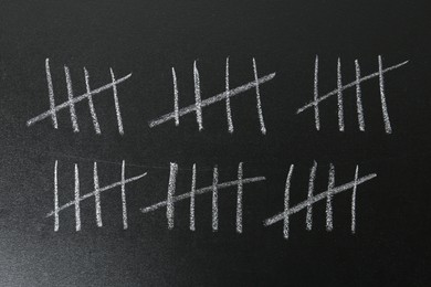 Photo of Counting days by drawing sticks with chalk on blackboard, closeup