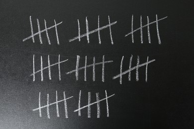 Photo of Counting days by drawing sticks with chalk on blackboard, closeup