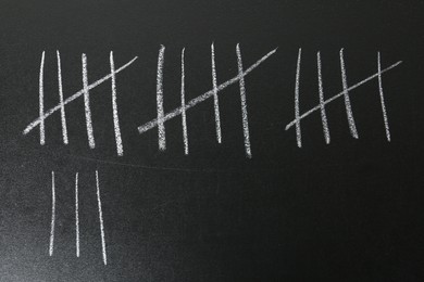 Photo of Counting days by drawing sticks with chalk on blackboard, closeup