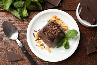 Photo of Tasty pudding with peanuts, mint and pieces of chocolate served on wooden table, flat lay