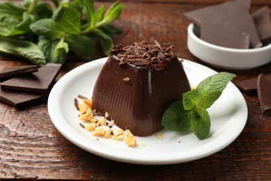 Photo of Tasty pudding with peanuts, mint and pieces of chocolate on wooden table, closeup