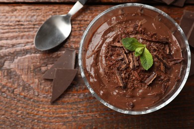 Photo of Tasty pudding with mint and pieces of chocolate served on wooden table, flat lay