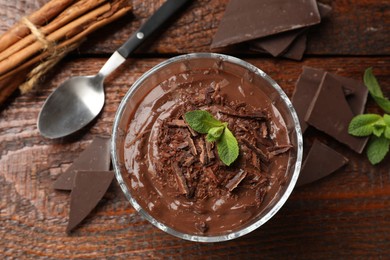 Photo of Tasty pudding with mint and pieces of chocolate served on wooden table, flat lay