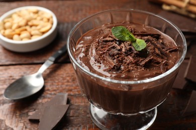 Photo of Tasty pudding with mint and pieces of chocolate served on wooden table, closeup