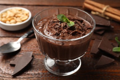 Photo of Tasty pudding with mint and pieces of chocolate served on wooden table, closeup