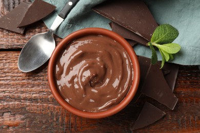 Photo of Tasty pudding with mint and pieces of chocolate served on wooden table, flat lay