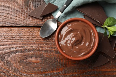 Photo of Tasty pudding with mint and pieces of chocolate served on wooden table, flat lay. Space for text