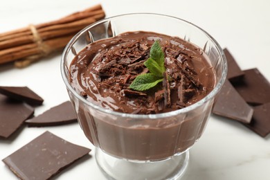 Photo of Tasty pudding with mint and pieces of chocolate on white table, closeup