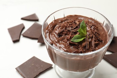 Photo of Tasty pudding with mint and pieces of chocolate on white table, closeup