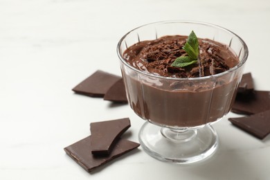 Photo of Tasty pudding with mint and pieces of chocolate on white table, closeup