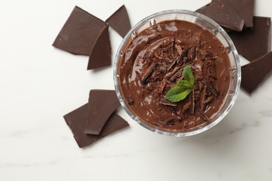 Photo of Tasty pudding with mint and pieces of chocolate on white table, flat lay