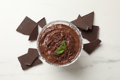 Photo of Tasty pudding with mint and pieces of chocolate on white table, flat lay