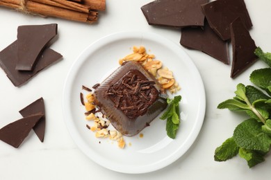 Photo of Tasty chocolate pudding with peanuts and mint on white table, flat lay