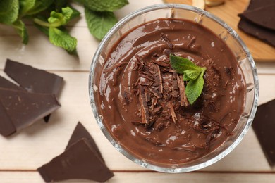 Photo of Tasty pudding with mint and pieces of chocolate on white wooden table, flat lay