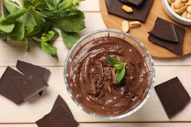 Photo of Tasty pudding with mint and pieces of chocolate on white wooden table, flat lay